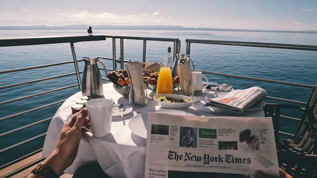man eating breakfast with newspaper and view of water